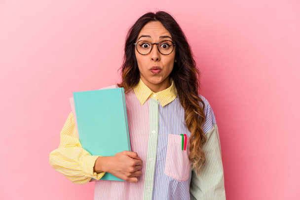Young student mexican woman isolated on pink background shrugs shoulders and open eyes confused. - Foto, Imagen
