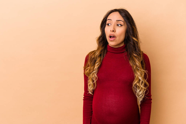 Jeune mexicaine enceinte isolée sur fond beige étant choquée à cause de quelque chose qu'elle a vu. - Photo, image