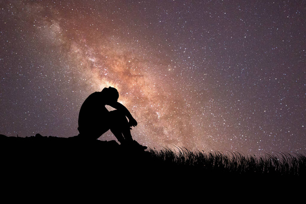 Un homme est assis déçu amoureux de la Voie lactée et des étoiles en arrière-plan. concept de perte, de solitude, de déception - Photo, image
