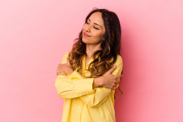Young mexican woman isolated on pink background hugs, smiling carefree and happy. - Photo, Image