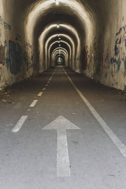 Ok işaretli dar bir tünel. Aydınlatma ve yön işareti olan boş bir tünel. Seyahat yerleri kavramı. İspanya, Camino de Santiago 'daki tünele giriş. Yol kavramı. Hedef ve hedef kavramı. - Fotoğraf, Görsel