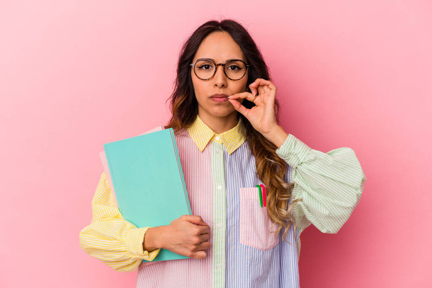 Young student mexican woman isolated on pink background with fingers on lips keeping a secret. - 写真・画像