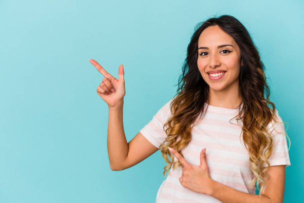Молода мексиканка ізольована на синьому фоні, збуджена, вказуючи на палець
. - Фото, зображення