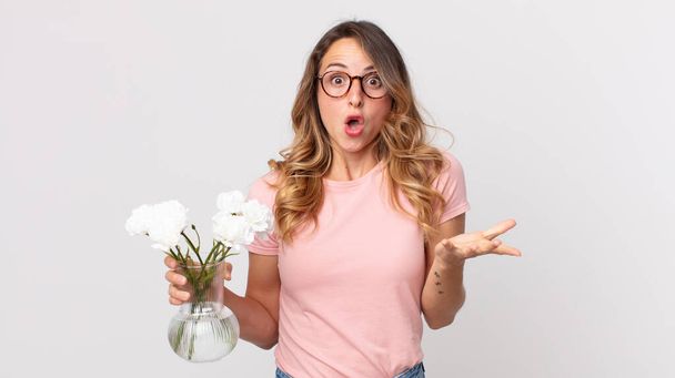 pretty thin woman feeling extremely shocked and surprised and holding decorative flowers - Foto, Bild