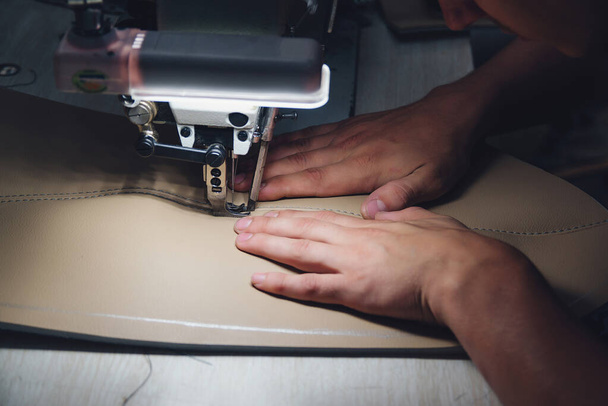 Arbeitsprozess des Lederhandwerkers. Gerber näht Leder in Großaufnahme an einer speziellen Nähmaschine. Arbeiter nähen Lederwaren auf der Nähmaschine. Werkstatt für Lederarbeiter. - Foto, Bild