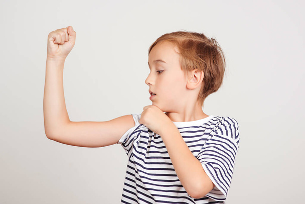 Cute boy showing his arm muscle. Childhood, fitness and sports. Funny child posing at studio. Success, motivation and win concept. School boy showing strength and power. - Photo, Image