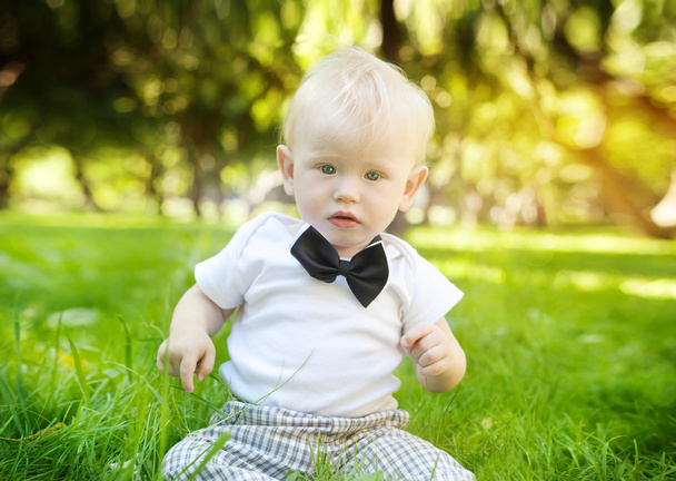 funny little boy sitting on the grass in the park - Photo, Image
