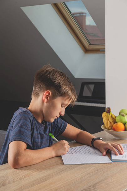 Chłopiec odrabia lekcje przy stole kuchennym z książką - Zdjęcie, obraz