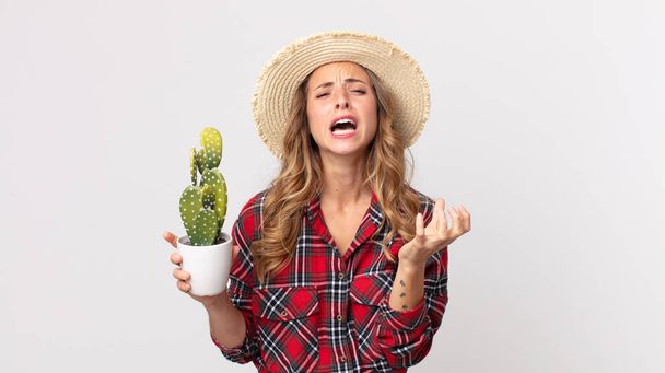 pretty thin woman looking desperate, frustrated and stressed holding a cactus. farmer concept - Foto, imagen