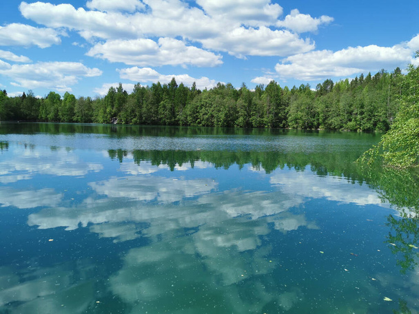 Brzeg jeziora jest jasny z czystą wodą, w której można zobaczyć marmur na dnie i odzwierciedlać niebo z chmurami, w parku górskim Ruskeala. - Zdjęcie, obraz