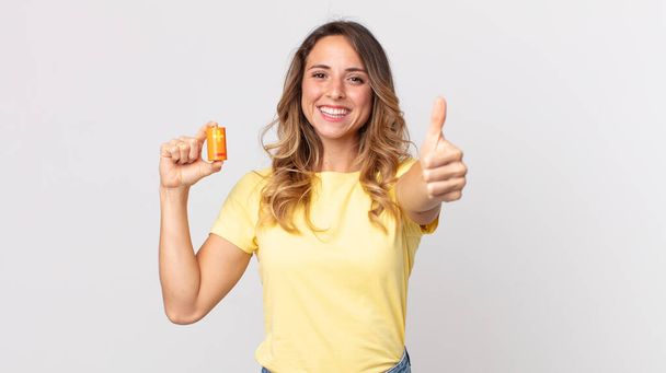 pretty thin woman feeling proud,smiling positively with thumbs up and holding batteries - Fotoğraf, Görsel
