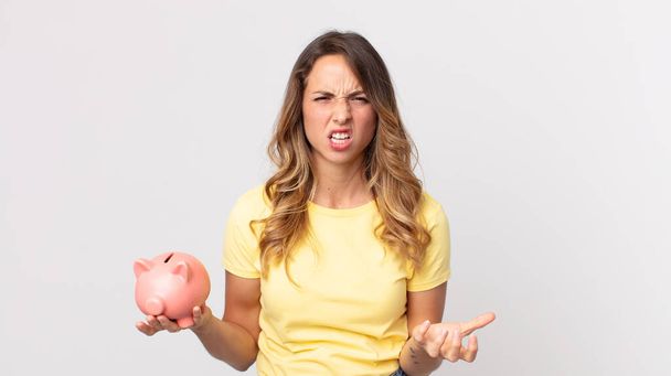 pretty thin woman looking angry, annoyed and frustrated and holding a piggybank - Foto, Imagem