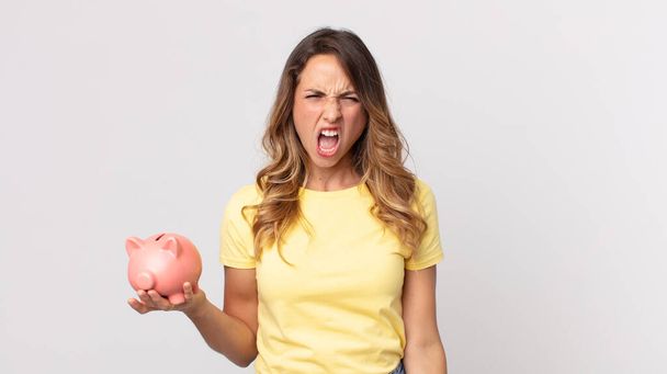 pretty thin woman shouting aggressively, looking very angry and holding a piggybank - Foto, Imagem