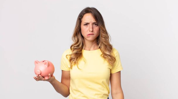 pretty thin woman looking puzzled and confused and holding a piggybank - Foto, Imagem