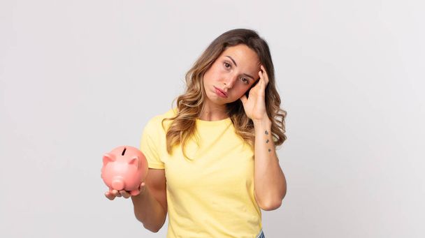 pretty thin woman feeling bored, frustrated and sleepy after a tiresome and holding a piggybank - Foto, Imagem