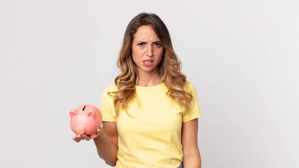 pretty thin woman feeling puzzled and confused and holding a piggybank - Фото, зображення