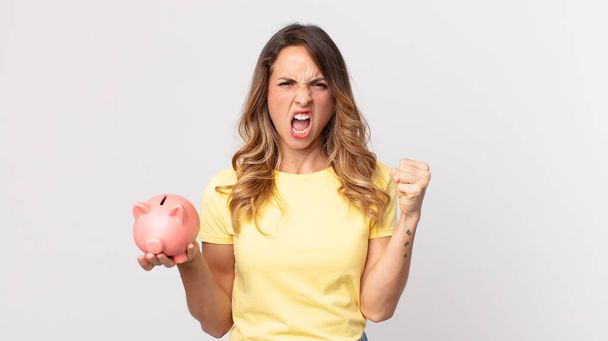 pretty thin woman shouting aggressively with an angry expression and holding a piggybank - Foto, afbeelding