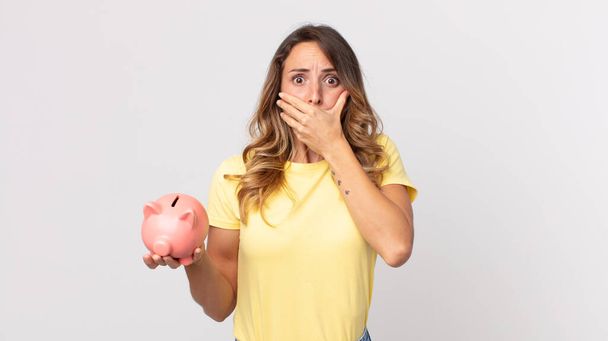 pretty thin woman covering mouth with hands with a shocked and holding a piggybank - Фото, изображение