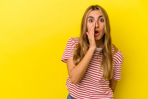 Young blonde caucasian woman isolated on yellow background is saying a secret hot braking news and looking aside - Photo, Image