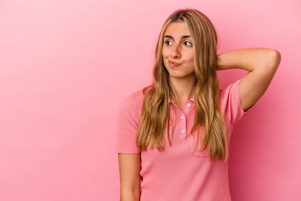Junge blonde kaukasische Frau isoliert auf rosa Hintergrund berührt Hinterkopf, denken und eine Wahl treffen. - Foto, Bild