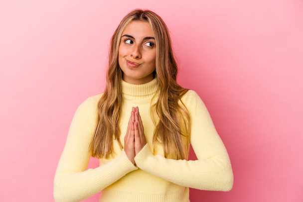Young blonde caucasian woman isolated on pink background praying, showing devotion, religious person looking for divine inspiration. - Photo, image