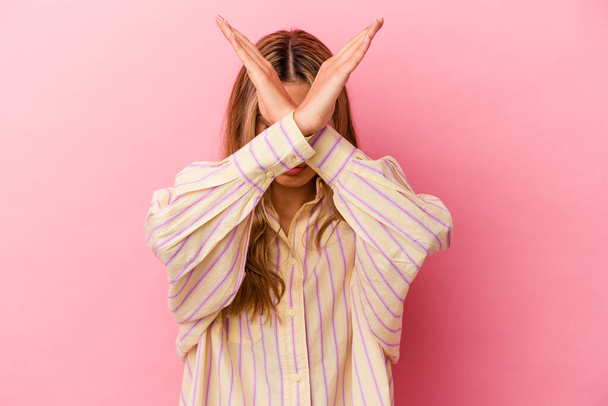 Young blonde caucasian woman isolated on pink background keeping two arms crossed, denial concept. - Foto, imagen