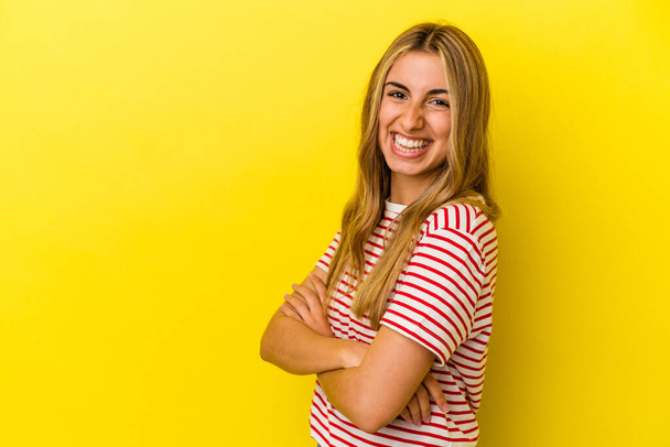 Jeune femme caucasienne blonde isolée sur fond jaune souriant confiant avec les bras croisés. - Photo, image