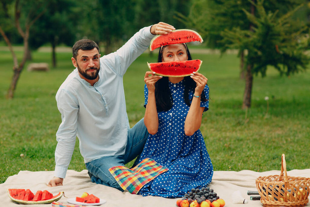 Young adult woman and man couple picnic at green grass meadow in park having fun with watermelon - Foto, afbeelding