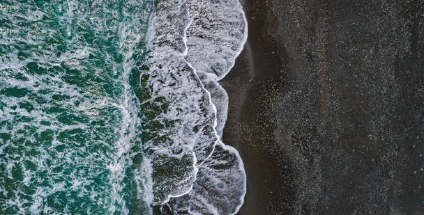 Sea shore with dramatic texture of breaking waves and black sand, drone perspective - Photo, Image