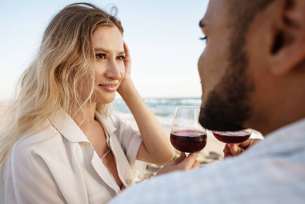 Portrait of a young couple sitting on the beach and drinking wine - Foto, Imagem
