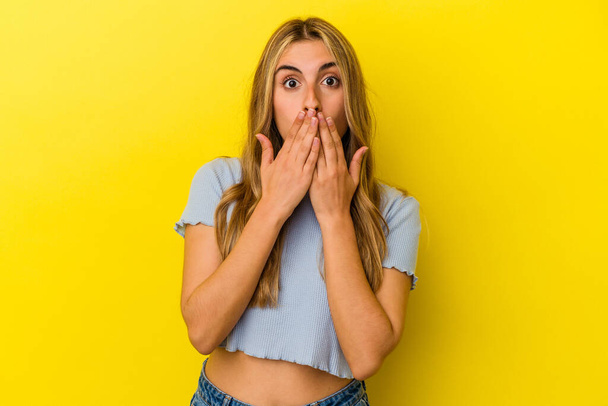 Mladá blondýnka běloška žena izolované na žlutém pozadí šokované pokrytí úst s rukama. - Fotografie, Obrázek
