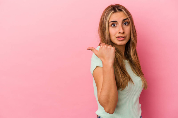Young blonde caucasian woman isolated on pink background points with thumb finger away, laughing and carefree. - Valokuva, kuva