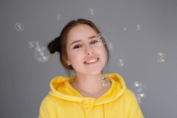 muotokuva viehättävä nuori nainen keltainen joukossa saippuakuplia kirkkaan harmaa tausta. Muodikas teini. trendikkäät värit - Valokuva, kuva