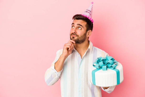 Young caucasian man celebrating his birthday isolated on pink background looking sideways with doubtful and skeptical expression. - Foto, Bild