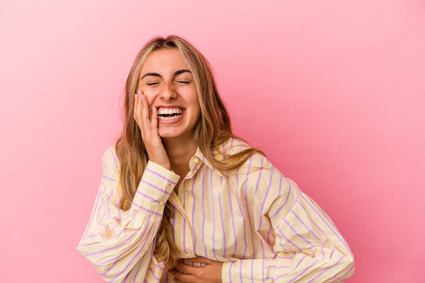 Mladá blondýnka běloška žena izolované na růžovém pozadí se šťastně směje a baví držet ruce na břiše. - Fotografie, Obrázek