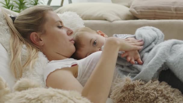 mamma felice coccola suo figlio bambino, sdraiato a casa tra i cuscini, sano e curato concetto di crescita  - Filmati, video