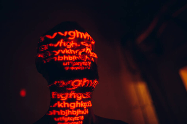 Jongeman met rode letters op zijn gezicht in het donker. - Foto, afbeelding