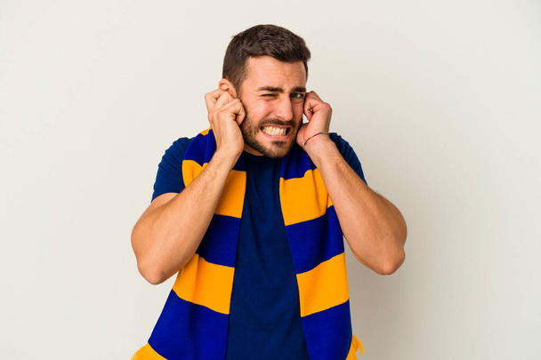Giovane tifoso caucasico di una squadra di calcio isolato su sfondo bianco che copre le orecchie con le mani. - Foto, immagini