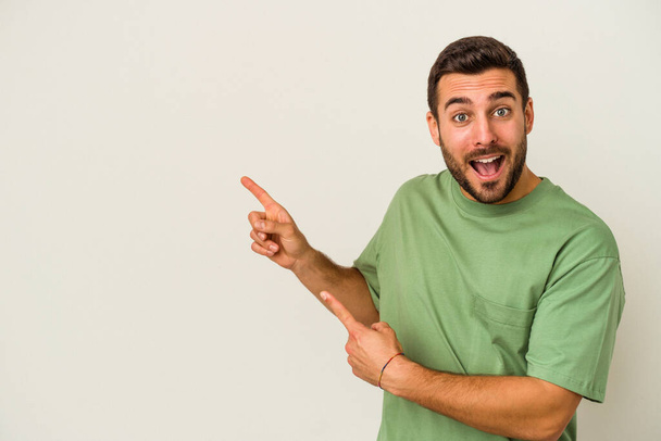 Junger kaukasischer Mann, isoliert auf weißem Hintergrund, zeigt mit den Zeigefingern auf einen Kopierraum und drückt damit Begeisterung und Sehnsucht aus. - Foto, Bild