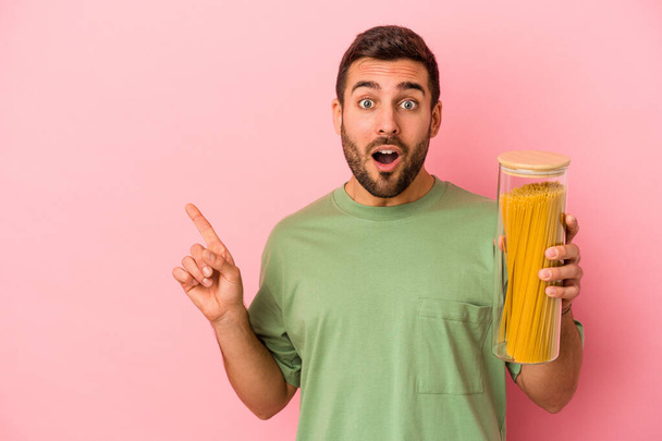 Young caucasian man holding pasta jar isolated on pink background pointing to the side - Foto, Imagem