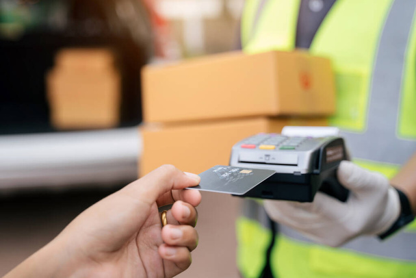 Close up of hand delivery man using credit card swiping machine to pay. Hand with creditcard swipe through terminal for payment on the outside of the warehouse, Select focus credit card. - Zdjęcie, obraz