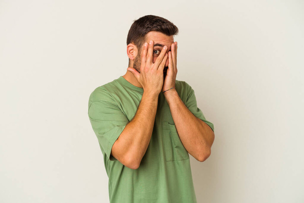Young caucasian man isolated on white background blink through fingers frightened and nervous. - 写真・画像