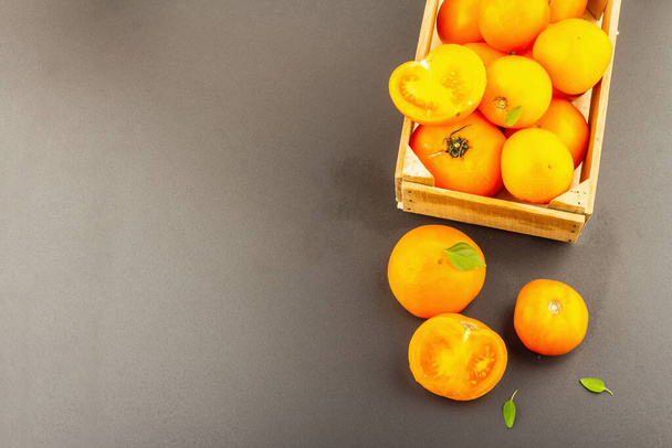 Kypsiä appelsiinitomaatteja ja tuoretta basilikaa. Uusi sato vihanneksia puinen laatikko. Musta kivi betoni tausta, ylhäältä - Valokuva, kuva