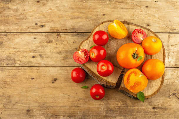 Assorted ripe tomatoes on a wooden stand. Fresh red and orange organic vegetables, basil leaves. Old wooden table, top view - Foto, imagen