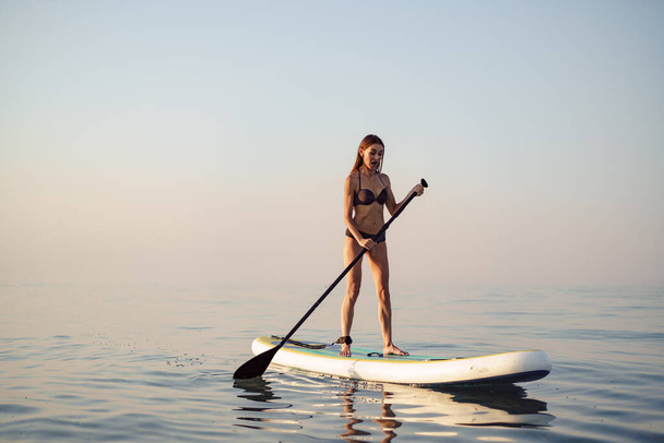 Young attractive woman standing on paddle board - Foto, Imagem
