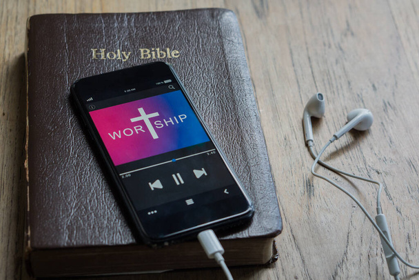 Bíblia com telefone e fones de ouvido, Conceito ouvir as palavras de Deus.Bíblia, telefone e fones de ouvido na mesa de madeira. - Foto, Imagem