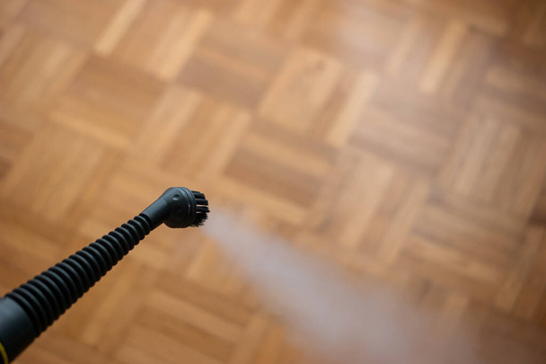 Steam pressure cleaner nozzle spraying water vapor cloud. Cleaning and disinfecting against germs and viruses Close up studio shot, no people. Wooden tile floor, shallow depth of field. - Foto, afbeelding