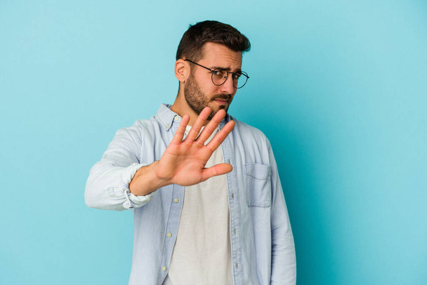 Young caucasian man isolated on blue background rejecting someone showing a gesture of disgust. - Foto, Bild