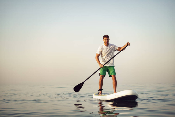 Young man in t-shirt and shorts floating on SUP board - Fotoğraf, Görsel