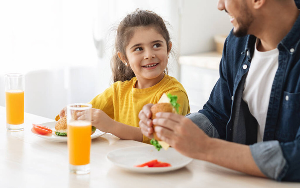 Portrait Of Happy Little Arab Girl Eating Sandwiches With Father In Kitchen - Foto, Imagem